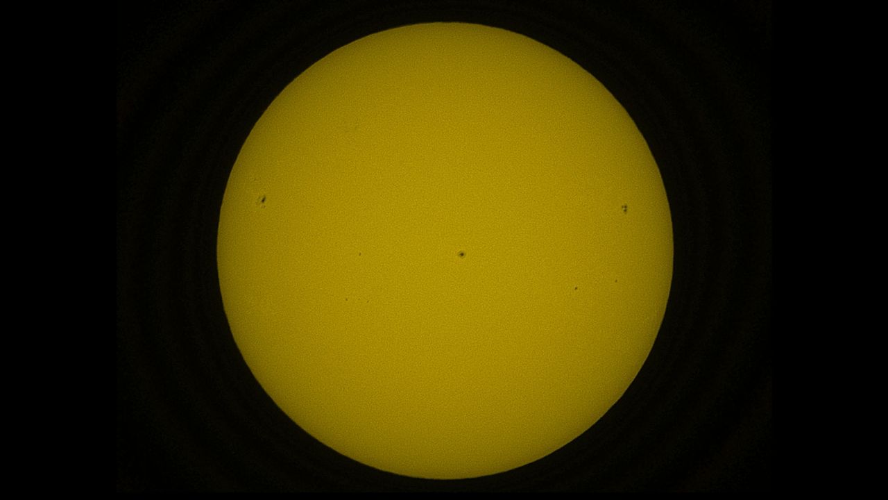 The solar disk in orange, showing dark sunspots.