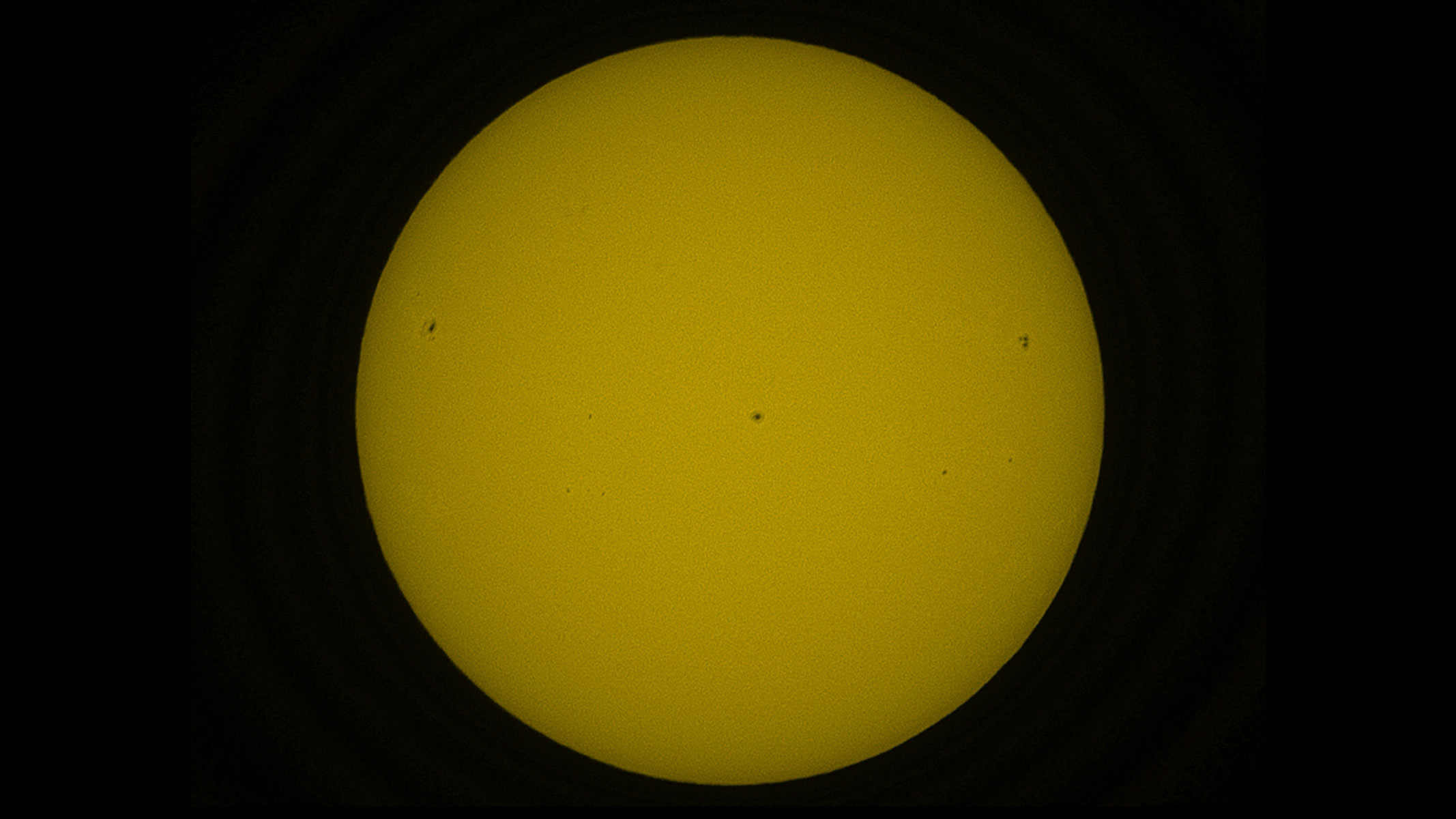 The solar disk in orange, showing dark sunspots.