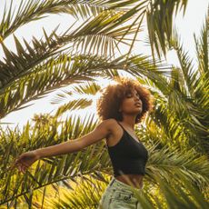 Woman with afro hair walking through palm trees in the sunshine