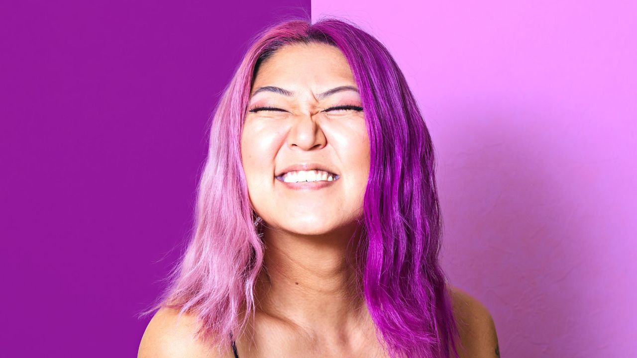 A Korean woman with pink and purple hair grins at the camera, gemini hair