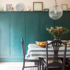 A dining room with green-painted wall panelling in a shaker style