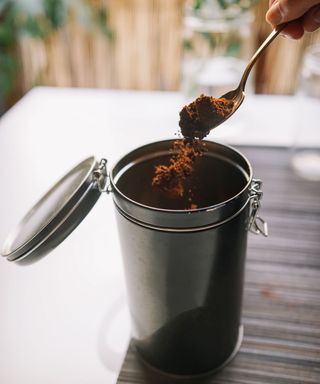 A silver tin with coffee grounds being taken out with a spoon