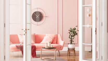 a salmon pink sofa in a pink paneled living room with wooden floors and white French doors