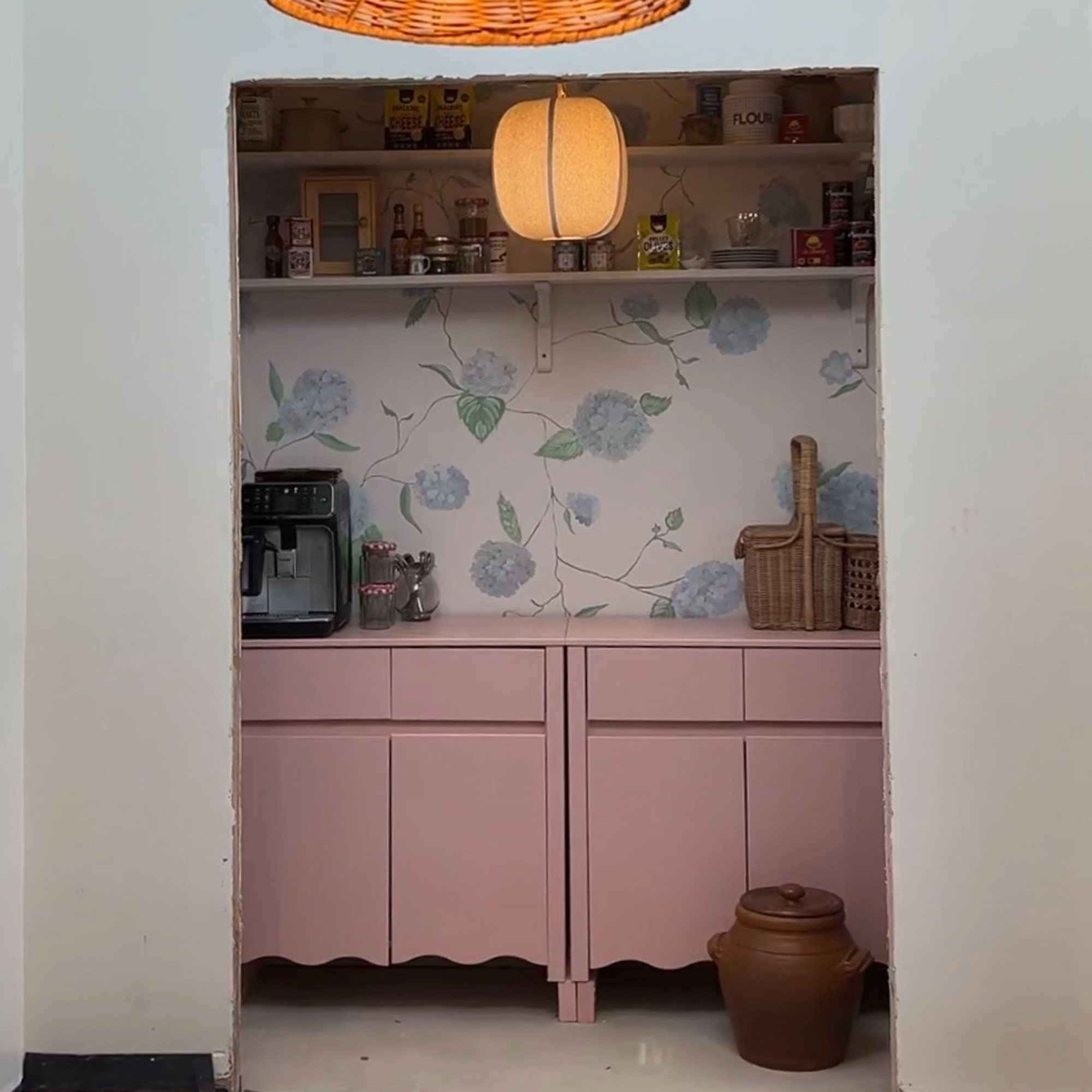 Small pantry ares with pink cabinetry, open shelving and wall painted with blue hydrangea pattern