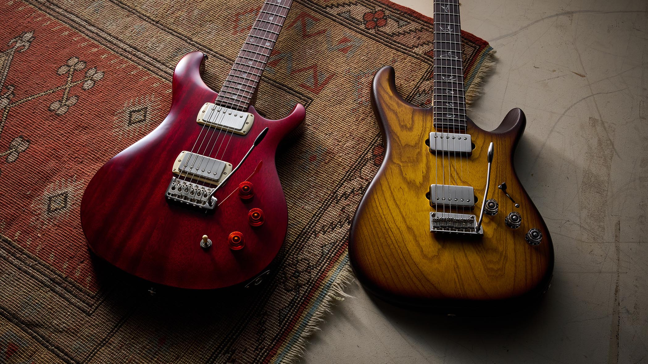 The PRS Fiore HH Satin and SE DGT Standard are pictured together on a rug