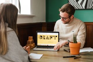 man showing a laptop with the word 'Craft' on it to a woman