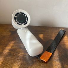 Blueair AlwaysCool Portable Handheld Fan laid horizontally with the head tilted forward on a wood-look sideboard