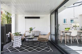 Sliding doors leading from dining area to covered outdoor decking with rattan garden furniture and monochrome outdoor rug