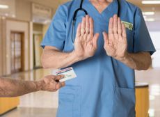 Senior doctor in scrubs refusing Medicare Card - stock photo