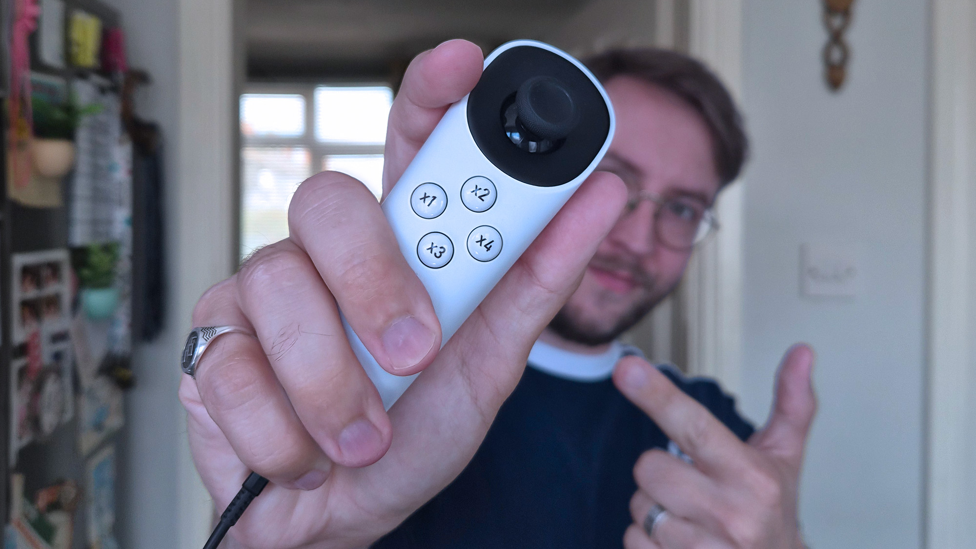 Ben Wilson of Windows Central holds a white Xbox Adaptive Joystick close to the camera, featuring a black thumbstick and four round buttons.