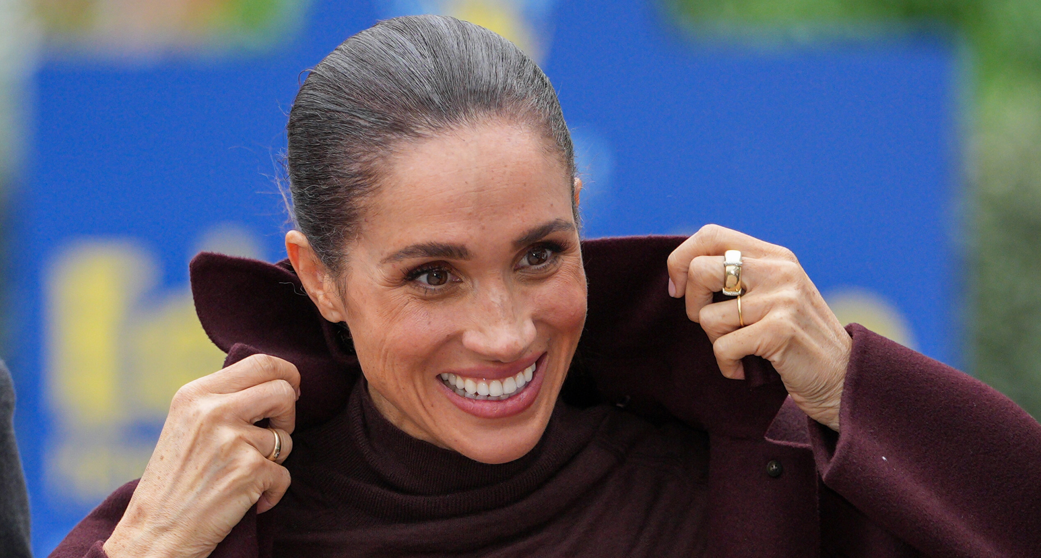 Meghan Markle pulling up the collar on her coat and smiling