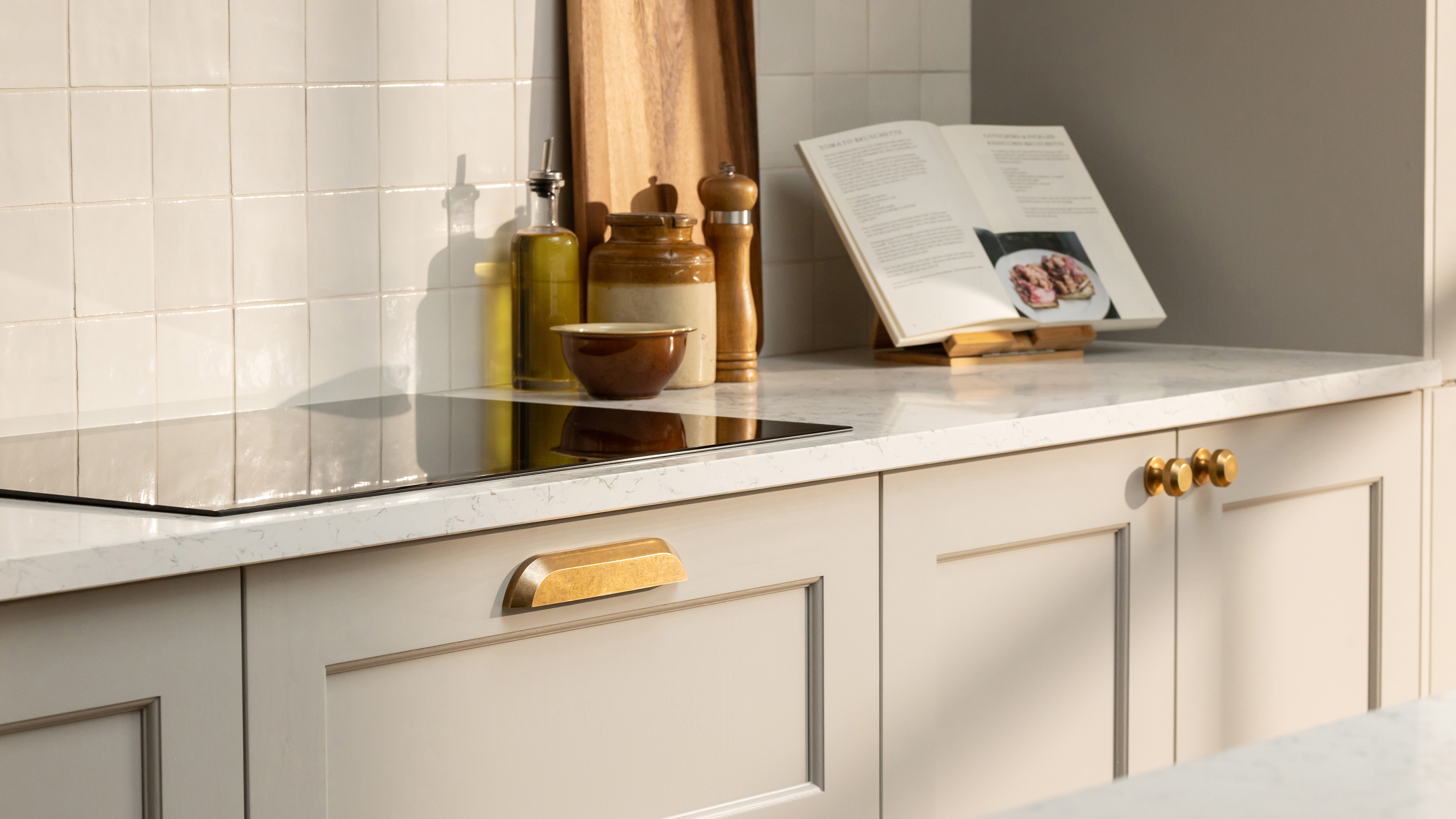 beige kitchen cabinets with gold statement drawer pulls and induction hob