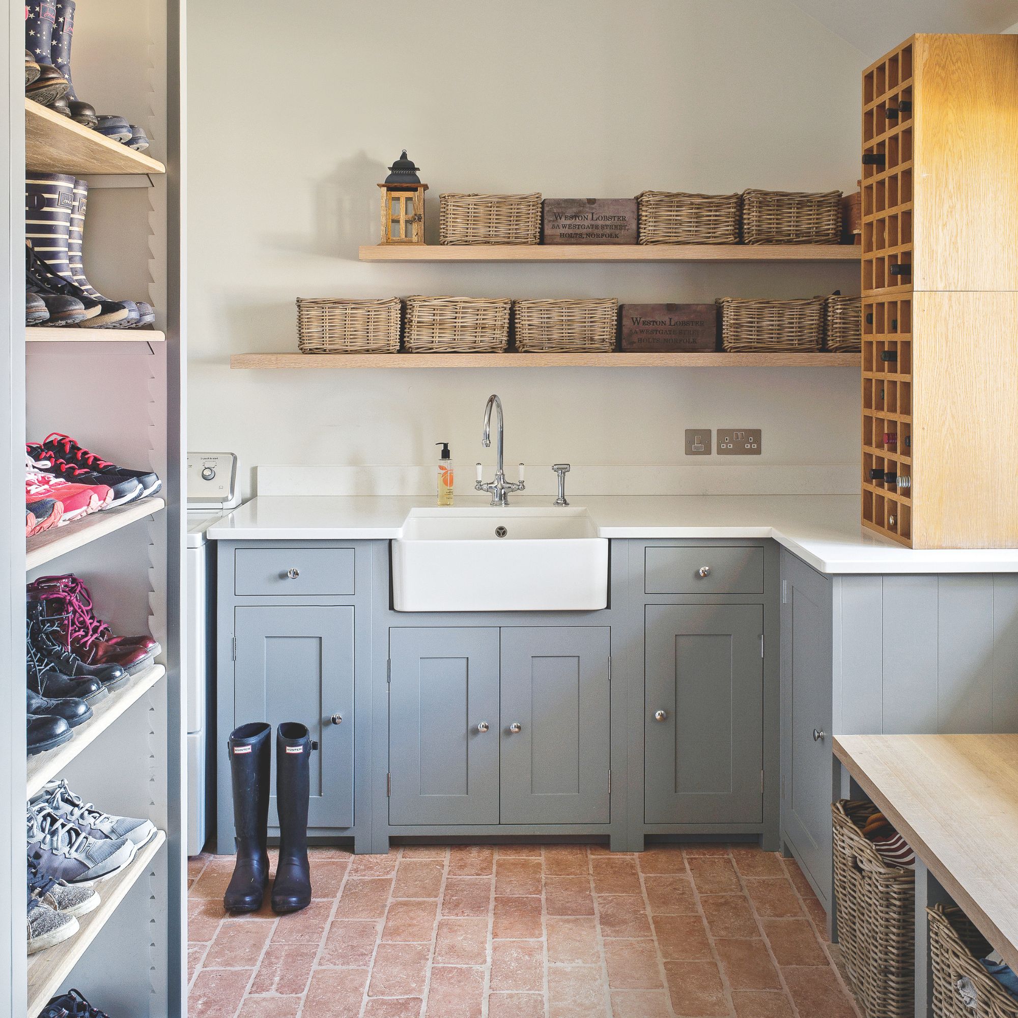 White painted boot room with blue cabinets and a white sink, with lots of storage baskets on the shelf above and shoes on shelves to the side