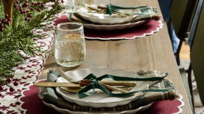 Wooden dining table with leafy centerpiece, red scalloped placemats, white scalloped crockery and green velvet bows