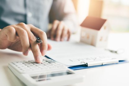 A person using a calculator next to a model of a home