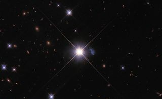 Tiny galaxy HIPASS J1131–31 peeks out from behind the glare of star TYC 7215-199-1, a Milky Way star positioned between Hubble and the galaxy.
