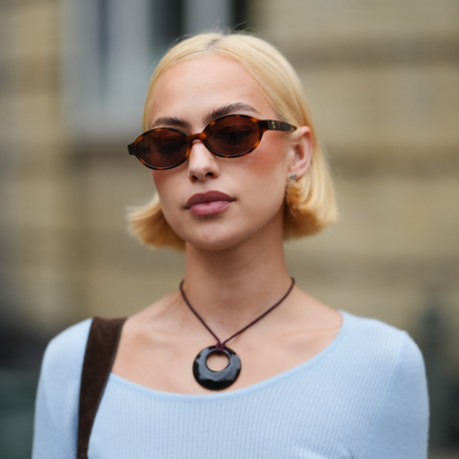 best brightening serums COPENHAGEN, DENMARK - AUGUST 04: A guest wears sunglasses with dark lenses and tortoiseshell frames. Hair is styled in a sleek, straight bob. Makeup includes defined eyebrows and a neutral lip color. A black circular pendant hangs from a thin cord necklace. 