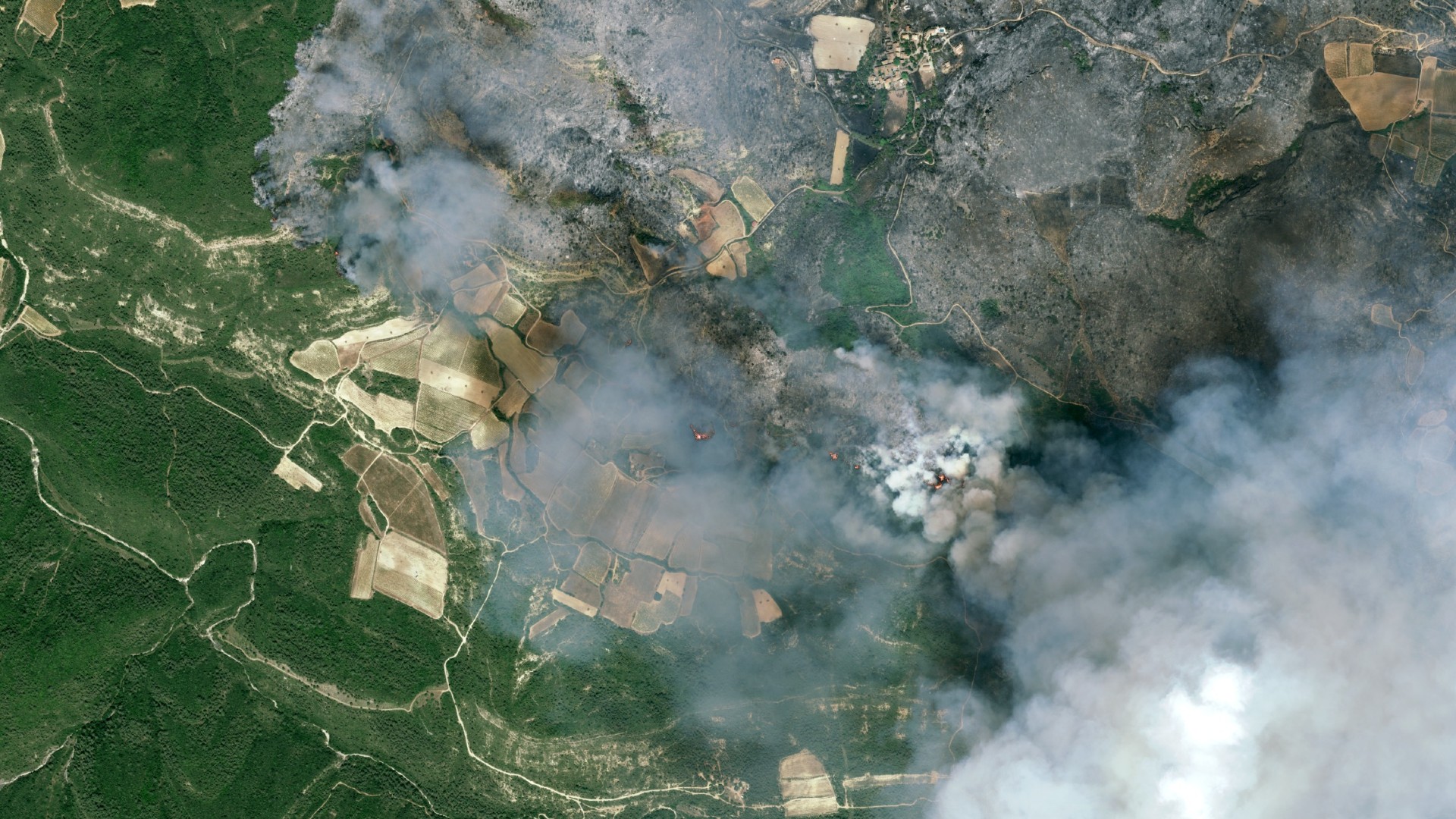 fire and smoke rolls through a green countryside as seen from space 