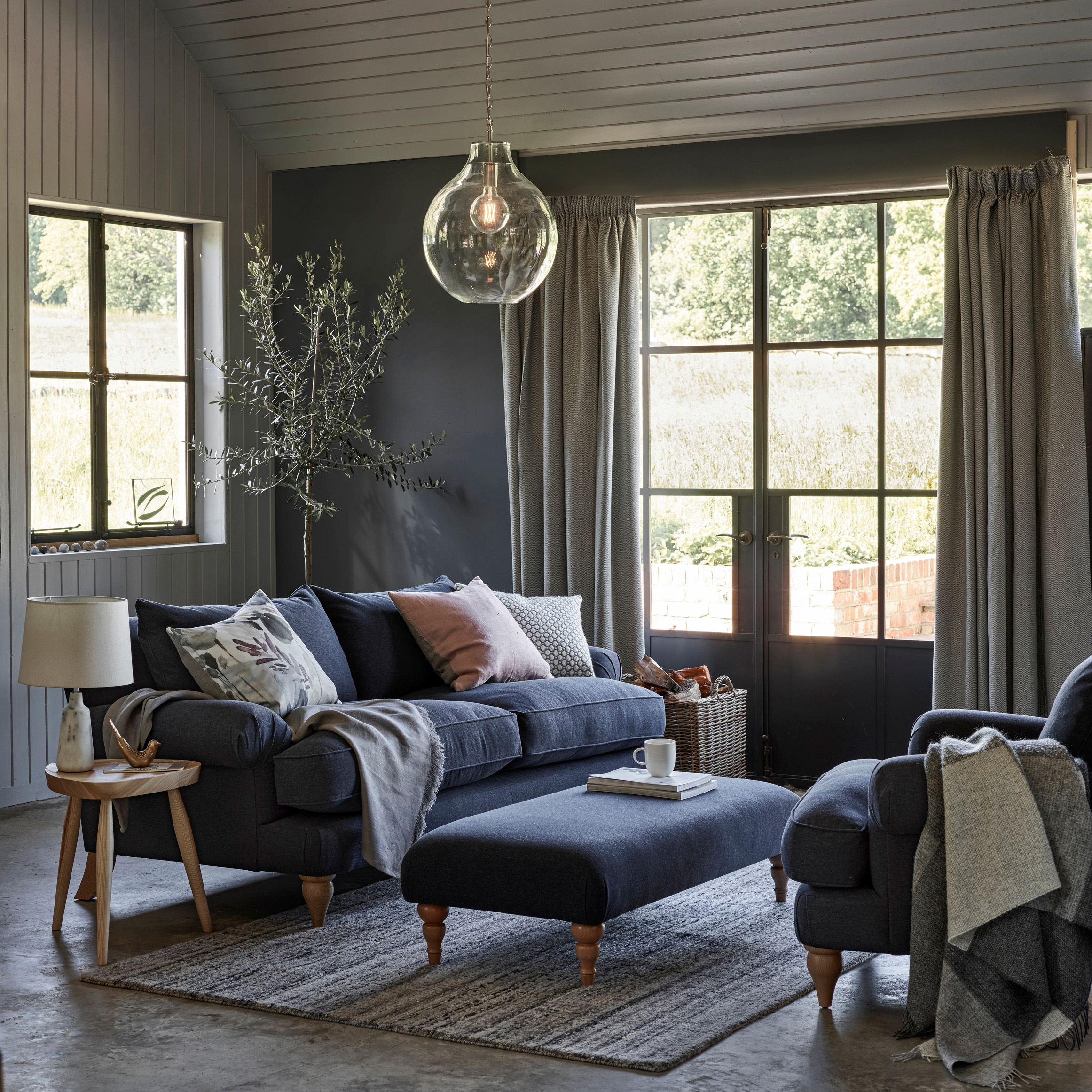 A modern rustic living room in grey from John Lewis with blue sofa and matching footstool, shiplap walls and ceiing and statement pendant light