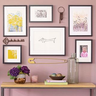 Purple wall with an arrangement of framed artwork and decorative objects above a wooden bench
