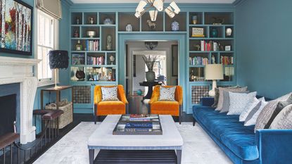 Living room, blue painted walls, pale grey rugs, pair of armchairs, sofa and built in bookshelves.