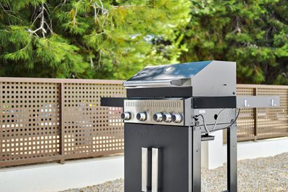 A stainless steel gas grill in a fenced off yeard