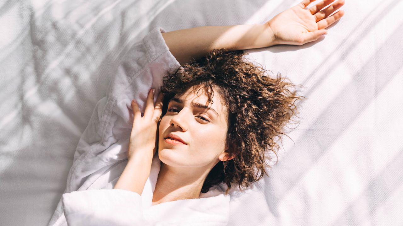 Best brightening serums - woman lying on a white sheets with face resting on her hand - getty images 1476124058