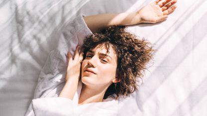 Best brightening serums - woman lying on a white sheets with face resting on her hand - getty images 1476124058