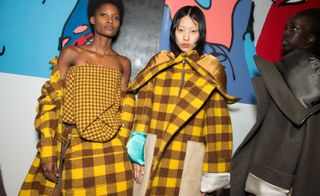 Both models can be seen wearing yellow and brown checkered clothing, from fold tops, oversized outerwear and shoulder bags