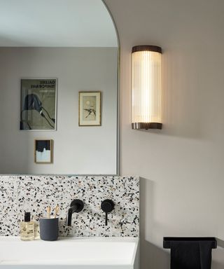 Modern bathroom with terrazzo tile backsplash, large mirror, wall light, artwork in mirror reflection, toothbrush holder, hand wash, black fixtures