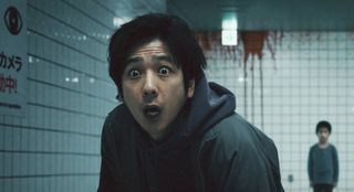 Kazunari Ninomiya in Exit 8, staring wide eyes at something while a little boy looms in the background. They are standing in a subway station with blood on the walls.