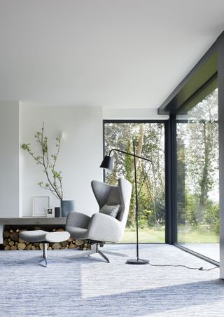 modern living room/sunroom with grey carpet and glass walls, grey armchair