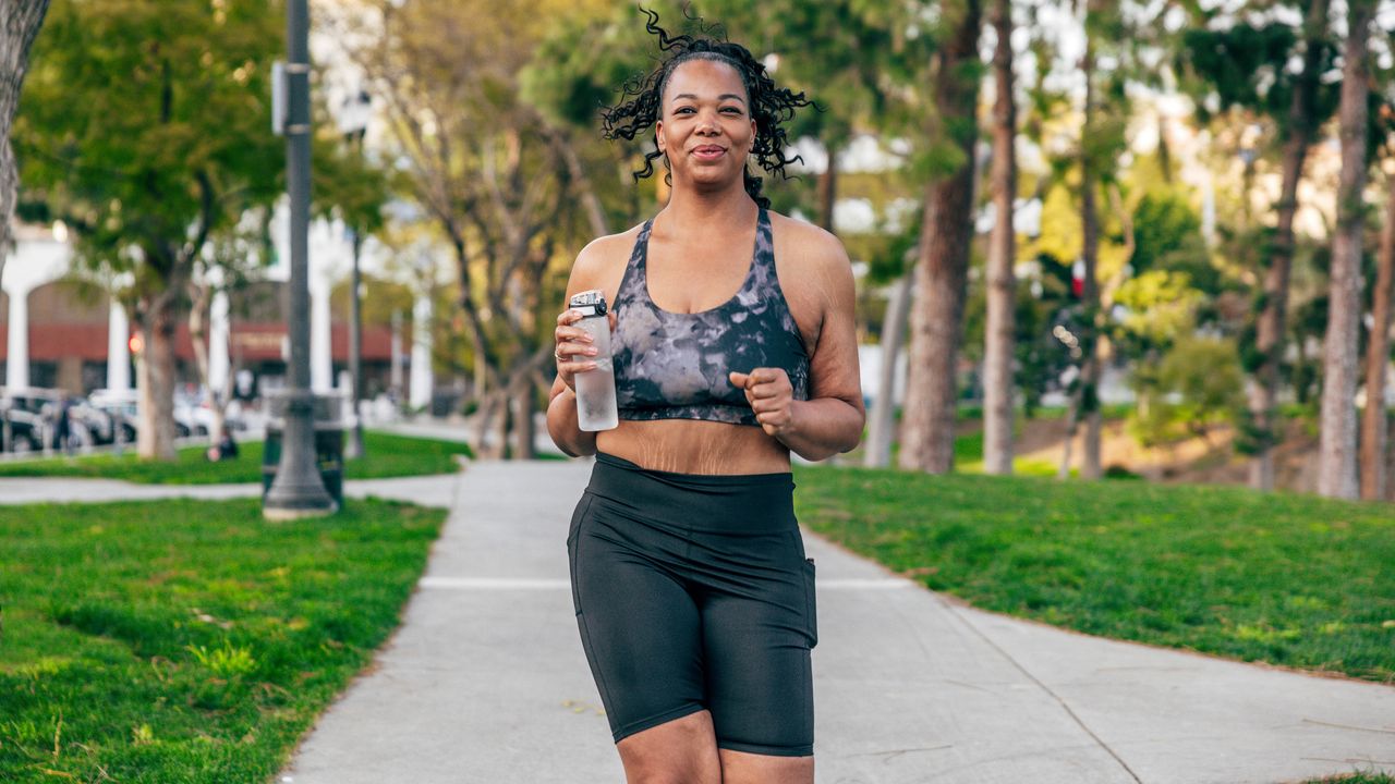 A woman running outdoors and holding a water bottle