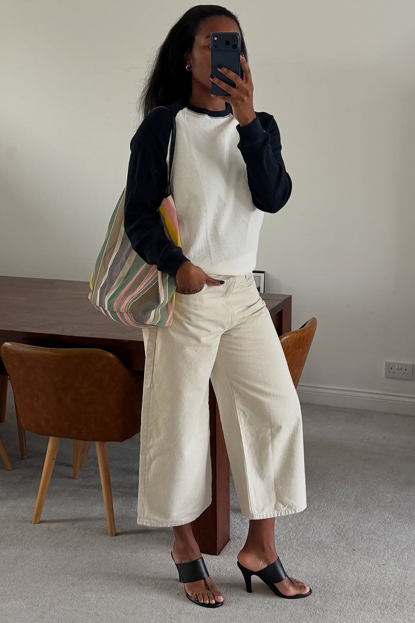 a woman wearing a longsleeve black and white shirt, white culottes pants, and black strappy heels