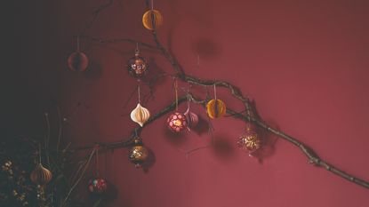 A tree branch decorated with Christmas ornaments set against a burgundy-painted wall