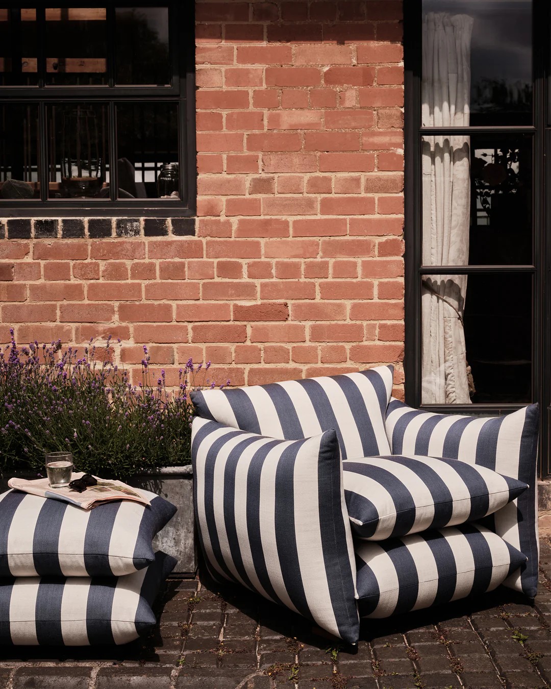 Image of an oversized blue and white striped chair and matching ottoman on the patio outside of a brick house