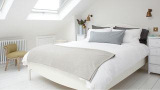 White attic bedroom with wooden double bed bedside cabinets and a small upholstered chair