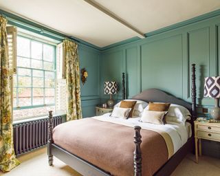 Main bedroom with blue green wood paneling and a double bed, floral curtains, wooden shutters
