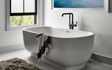 white bathtub with black tap and towel draped over edge