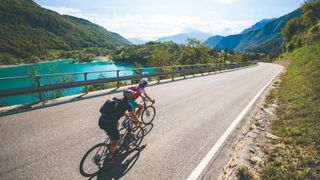 Image of two cyclists riding beside a stunning blue lake