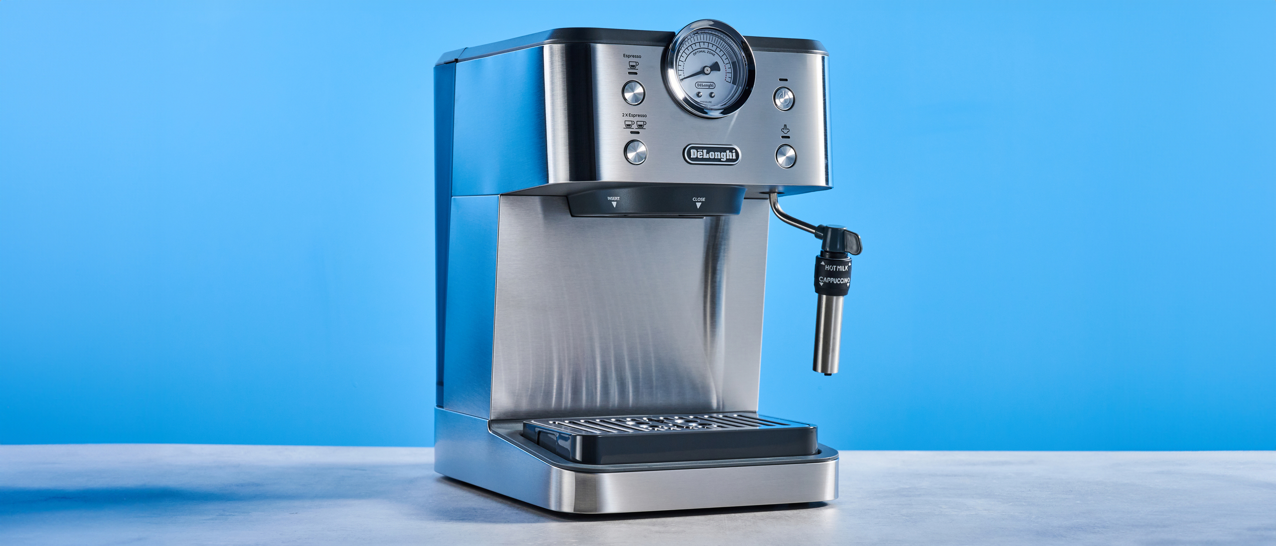 the De'Longhi Linea Classic espresso machine photographed against a blue tom's guide background, showing its silver finish, steam dial, steam wand, portafilter, and accessories