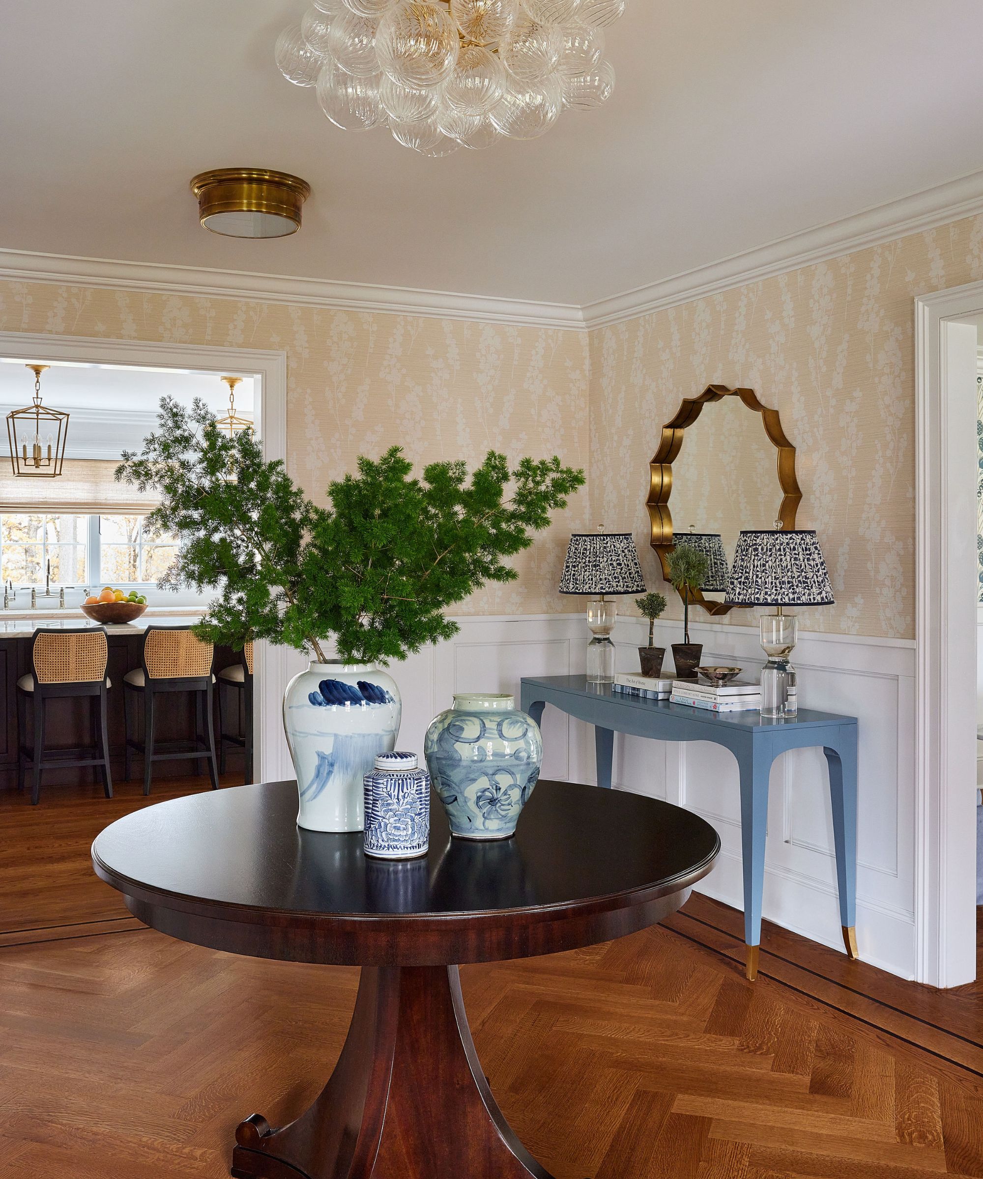 Traditional entryway with parquet flooring, a mahogany round table with a blue and white vase filled with foliage and smaller vases beside it, and a blue console table in the corner with lamps.