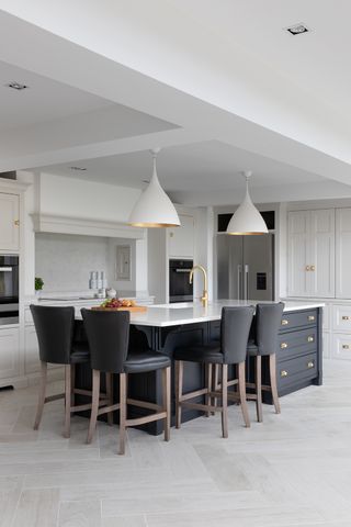 Planning a kitchen island with enough space around it, as shown in a white kitchen with white cabinetry, a gray kitchen island with white countertops and gray bar stools.