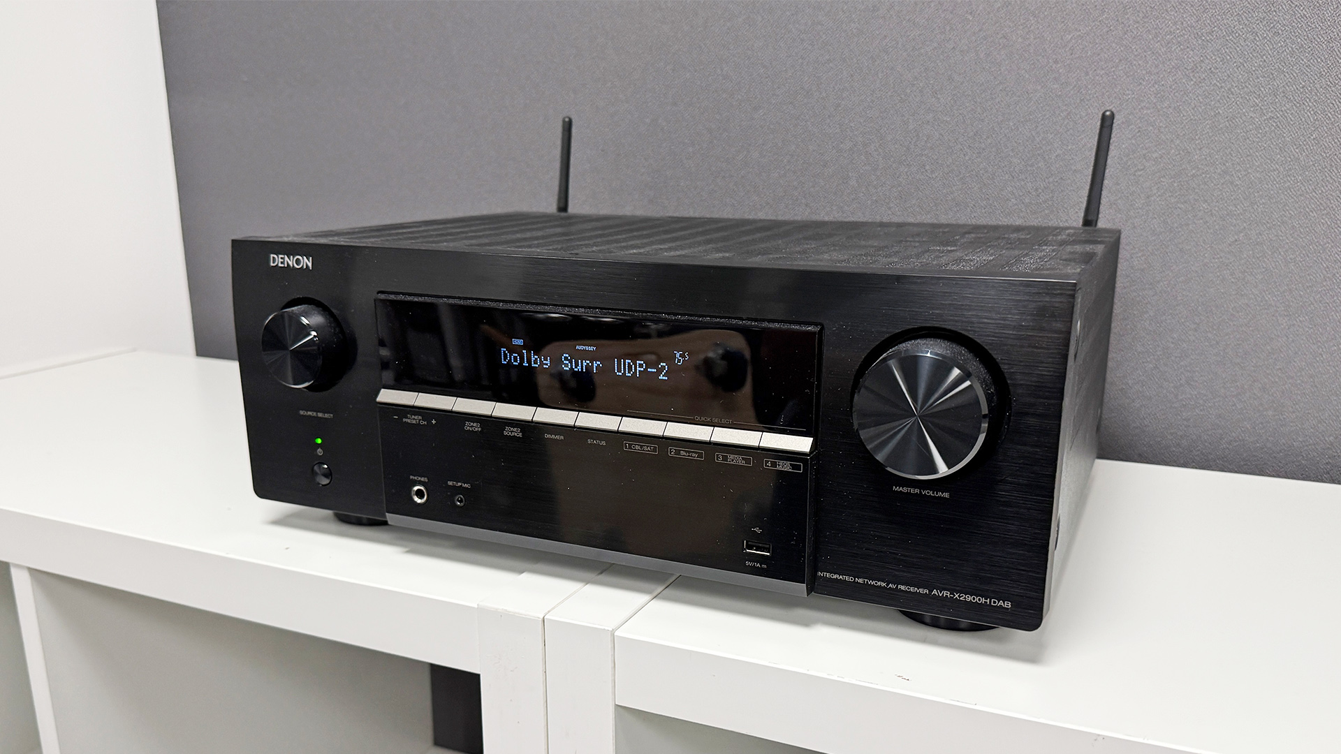 Denon AVR-X2900H home cinema amplifier on white shelving unit in front of grey baffle