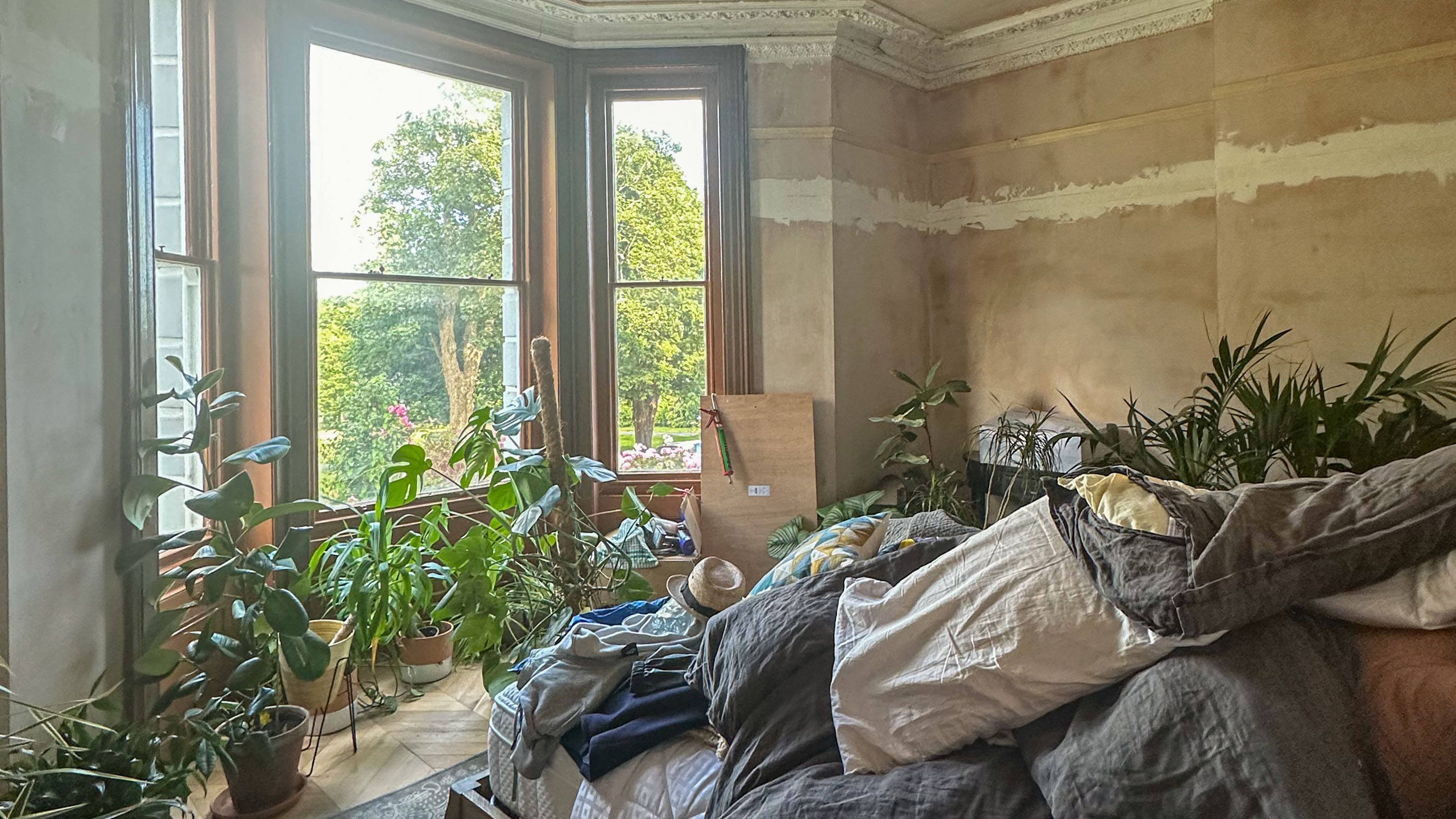 bedroom mid renovation with bare plaster walls and pillows piled on the bed