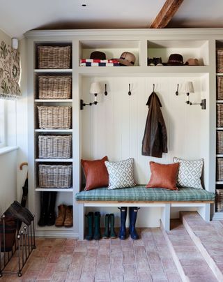 An example of mudroom ideas showing a cosy mudroom with a bench seat with cushions, wicker baskets and coat pegs
