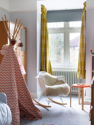 kids bedroom with a teepee, rocking chair, grey carpet and orange stool