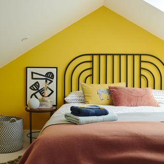 Bedroom with yellow feature wall, a black metal frame and yellow and pink bed linen