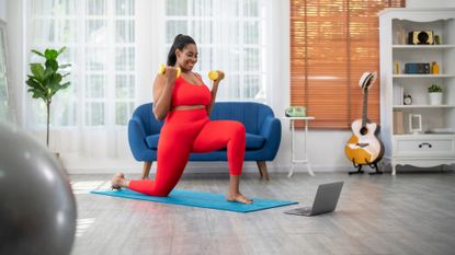 A woman performing a lunge and curl with dumbbells during a home workout