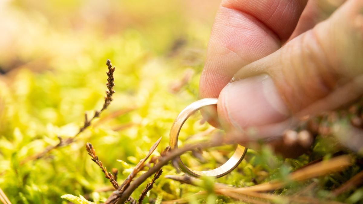 Man&#039;s hand lifting wedding ring out of moss